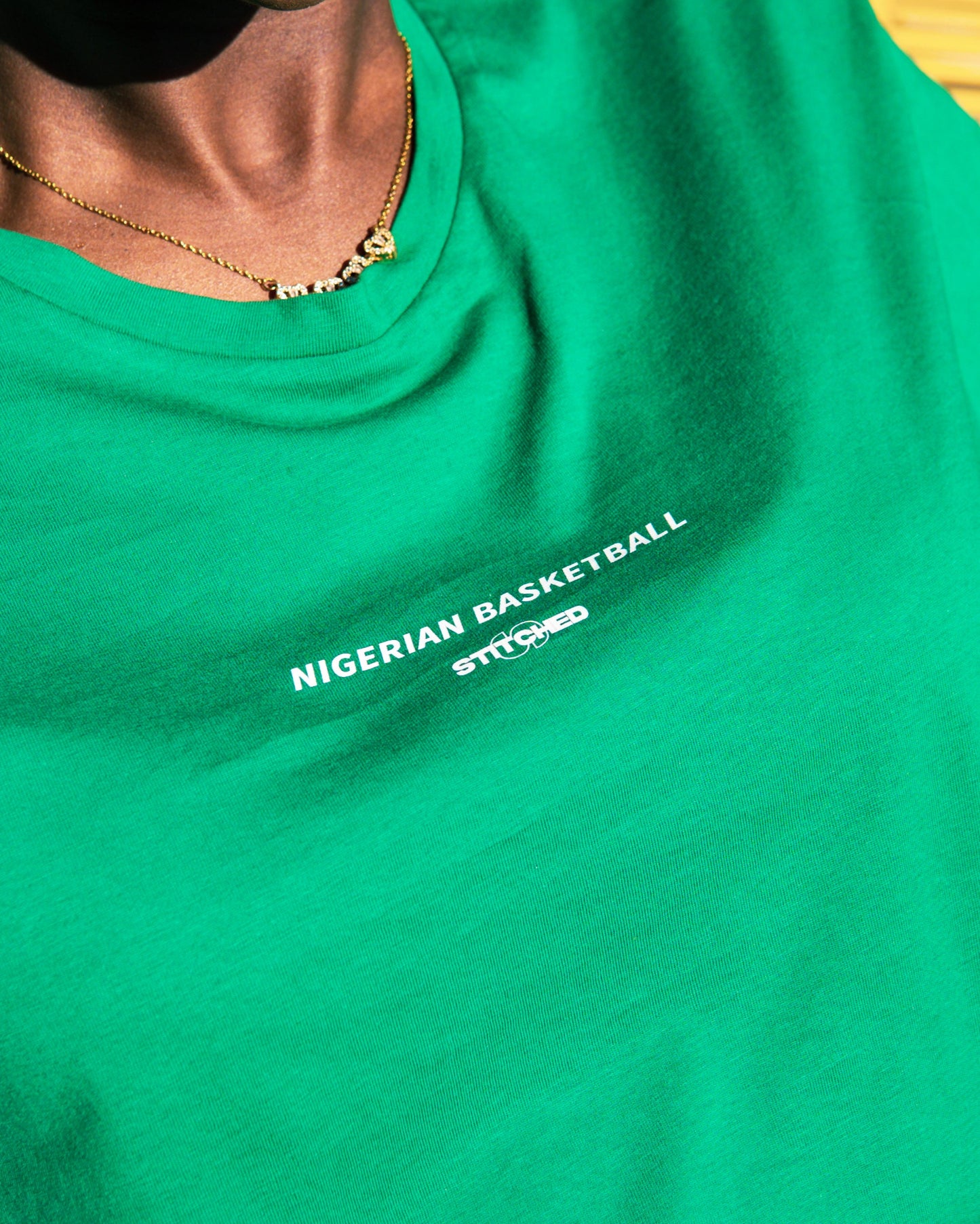 Front of green tee showing Nigerian Basketball × STITCHED chest print
