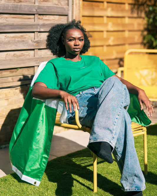 Woman wearing STITCHED Nigerian basketball tee seated in sun with flag over shoulders