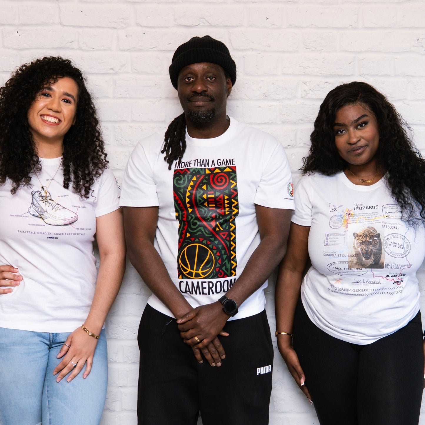 Three people wearing white t-shirts with various designs against a white brick wall.