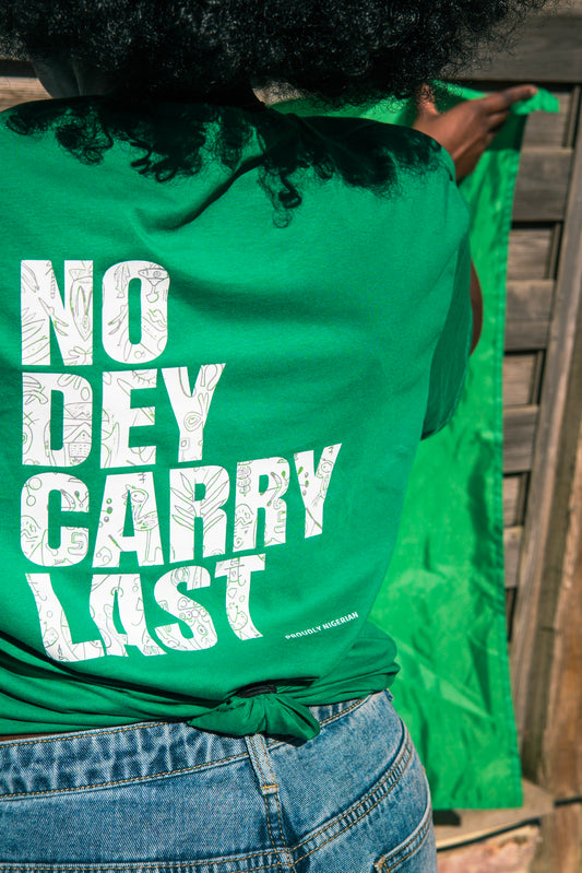 Back of green t-shirt with ‘No Dey Carry Last’ text, worn by model holding Nigerian flag